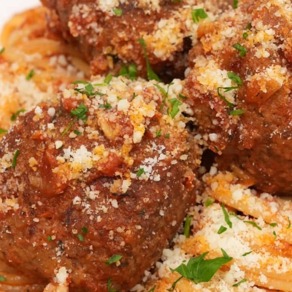 Close-up of San's meatballs and pasta, topped with grated cheese and fresh parsley.