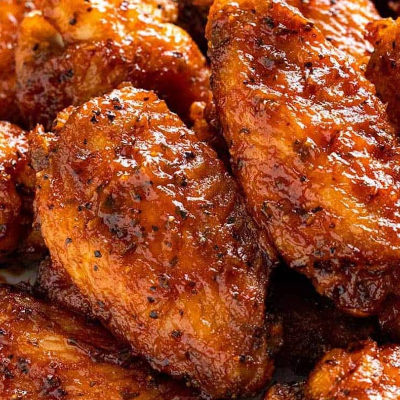 Close-up of several glistening, dark orange chicken wings with visible black pepper flakes.